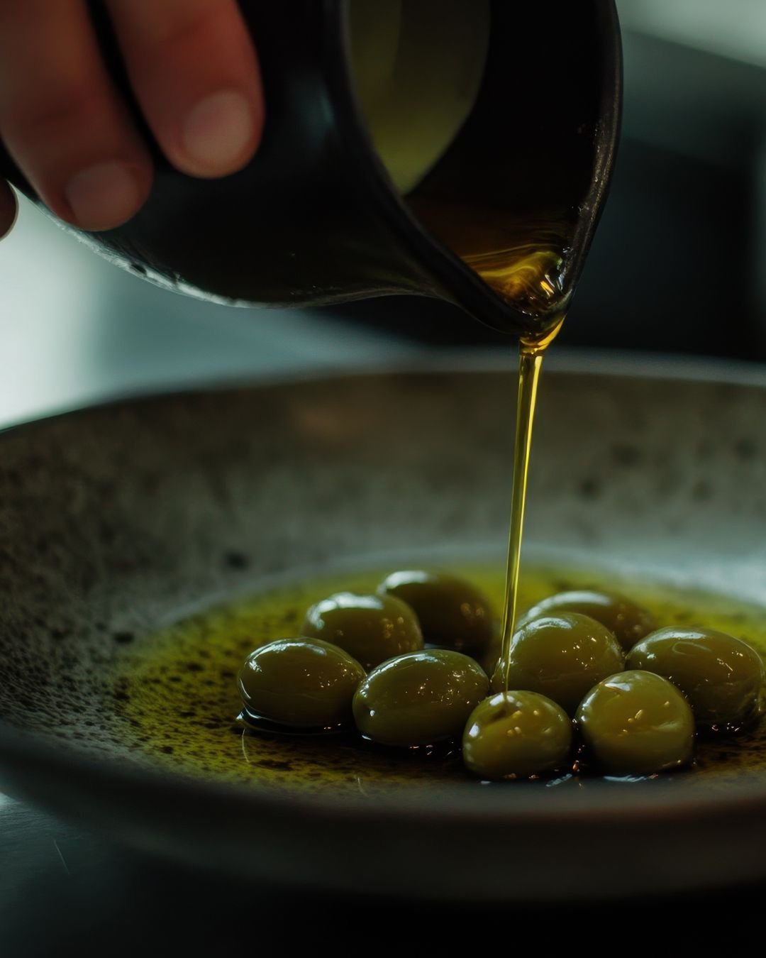Aceite de oliva vertiéndose sobre aceitunas verdes