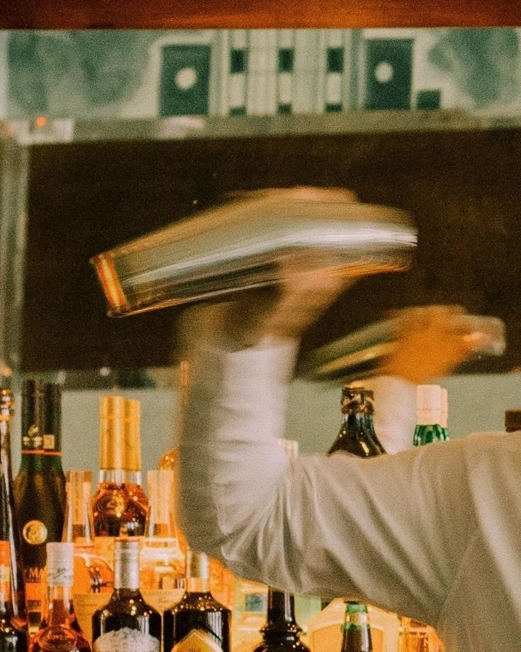 Bartender agitando una cocktelera en la barra entre botellas