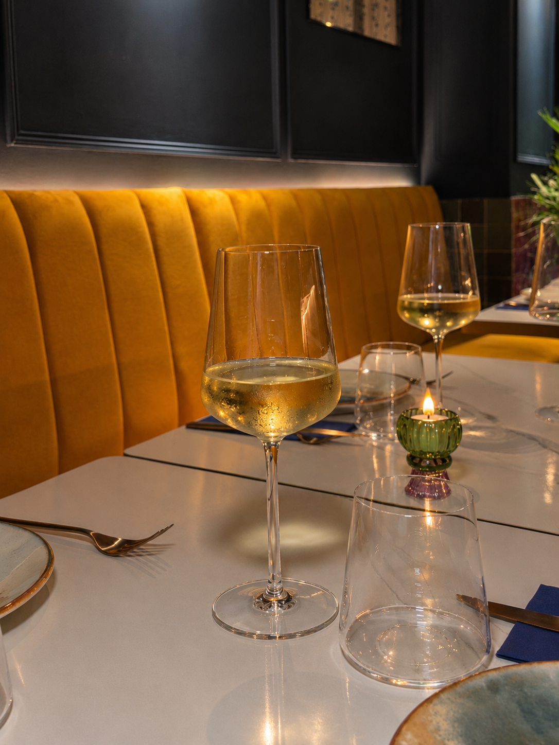Copa de vino blanco sobre la mesa con banqueta mostaza en AURA